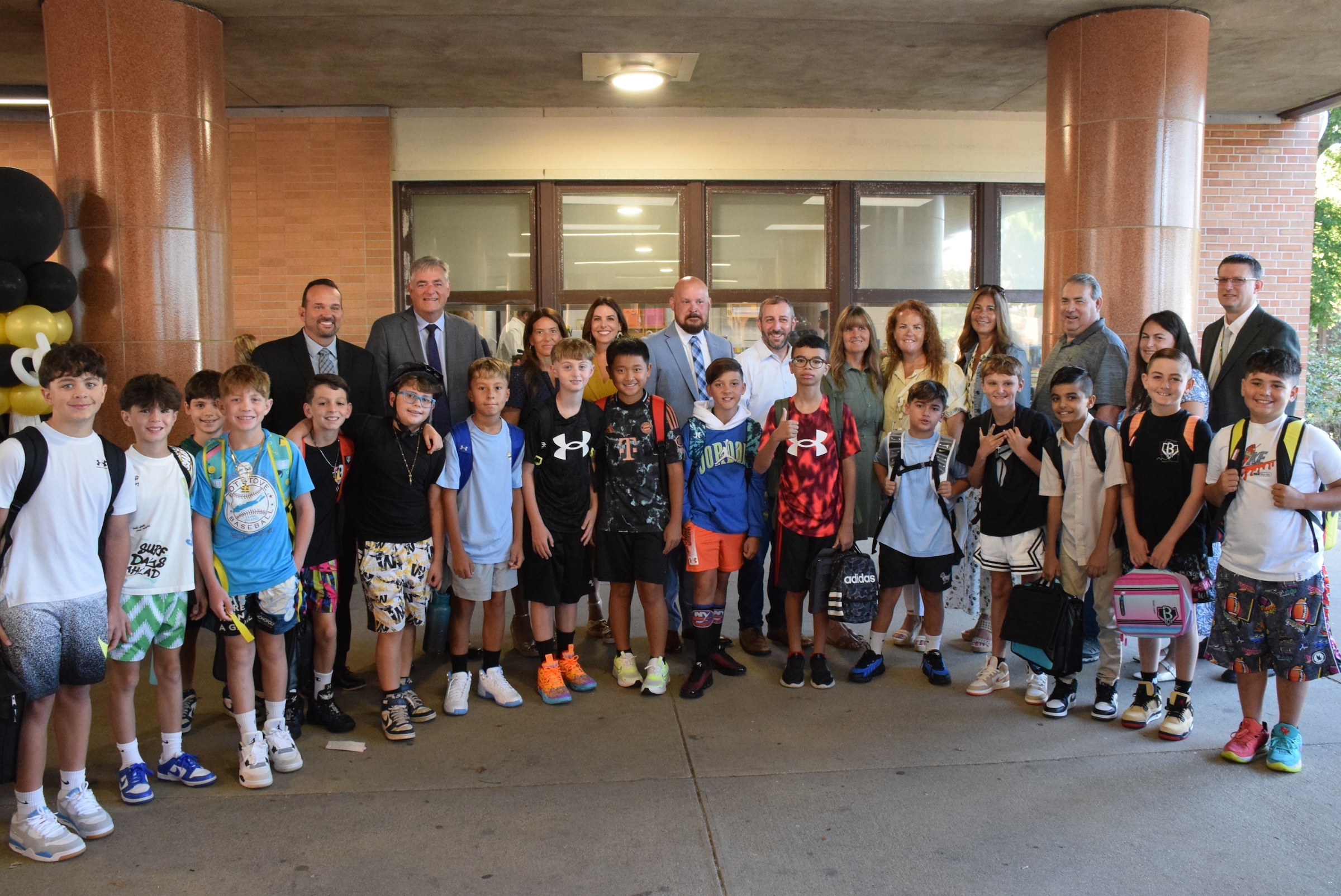 middle school students posing with district administrators outside of building
